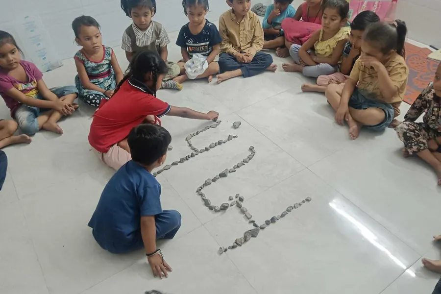 Children forming Gujarati letters in stones on the floor