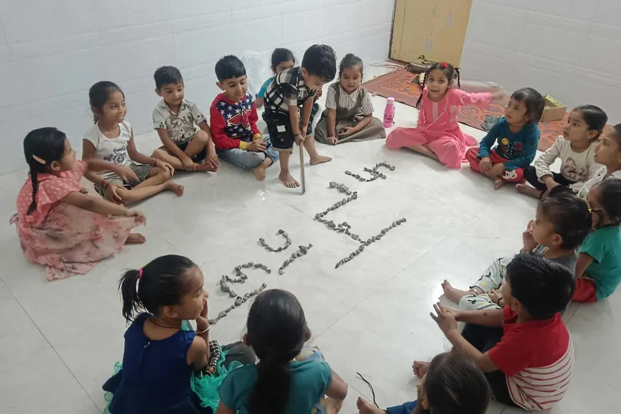 Children seated on the floor around letters laid out in small objects